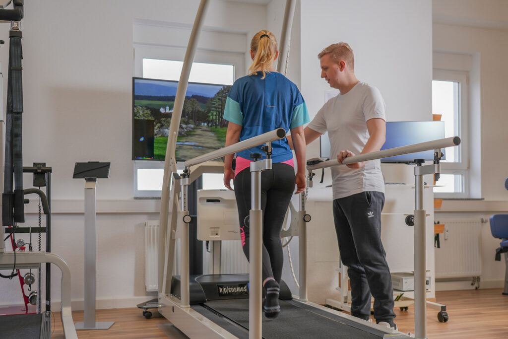 Physiotherapeut unterst&uuml;tzt Frau auf Laufband