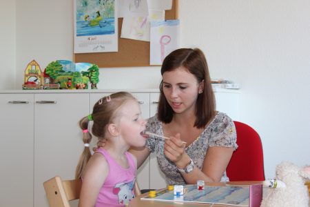 Logop&auml;die-Sitzung mit Logop&auml;din und Kind in heller Praxis