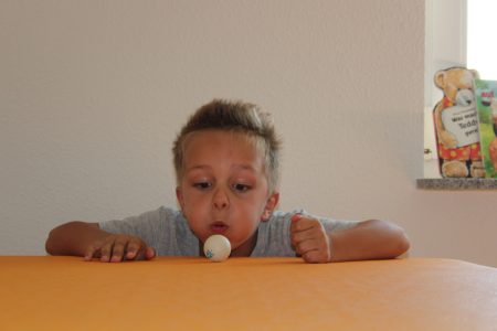 Junge bl&auml;st Tischtennisball auf orangem Tisch