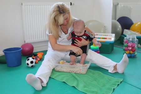 Physiotherapeutin hilft Baby auf Gymnastikmatte mit Sensorikschale