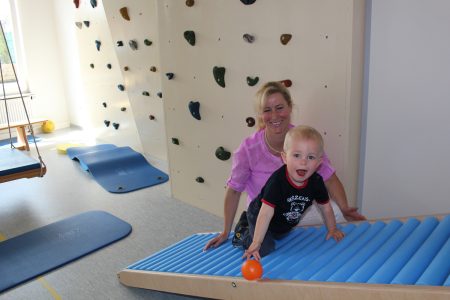 Kleinkind beim Klettern auf Indoor-Kletterwand mit Physiotherapeutin